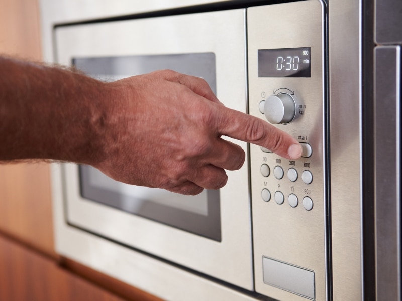 Person using control panel of built-in stainless steel oven comparing inverter microwave vs convection functions.