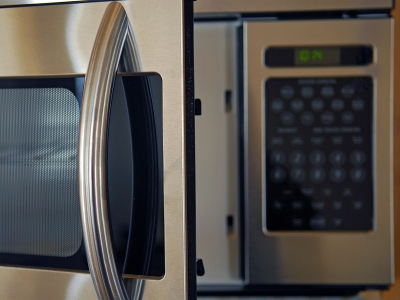Finger pressing start button on modern microwave control panel, showing different types of microwaves settings.
