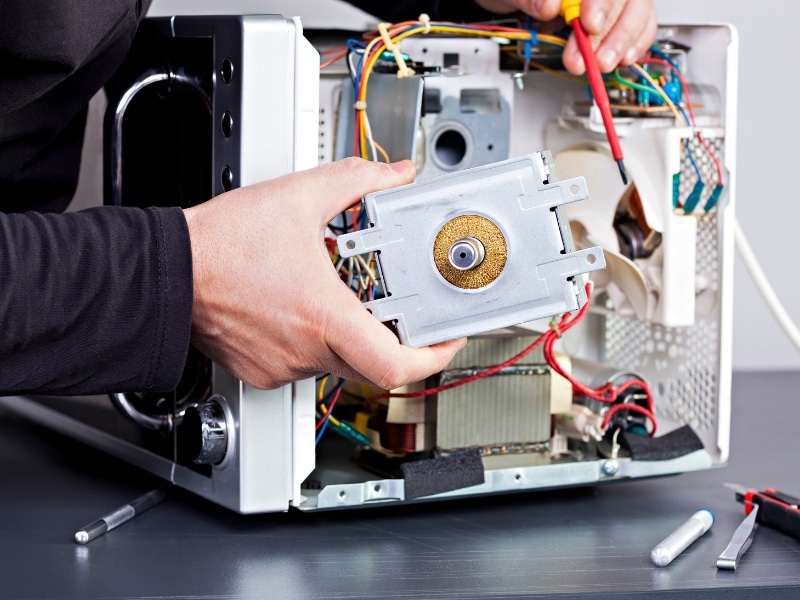 A technician removing internal components while inspecting parts of a microwave during a repair.