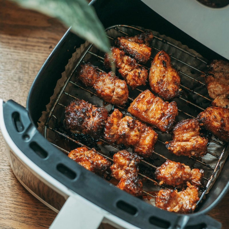 Air fryer basket with crispy glazed chicken wings cooking on metal rack.